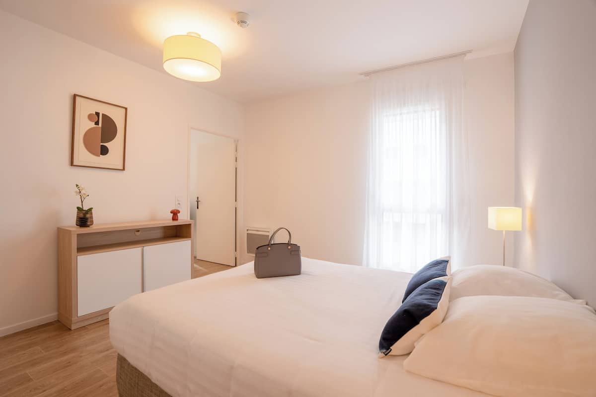 A bedroom with a bed, bedside table, lamp, and a framed picture on the wall.