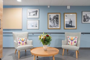 A lobby with two armchairs, a round wooden table, and a vase of flowers. - Quality Aparthotel Bourgoin-Jallieu (Bourgoin-Jallieu)
