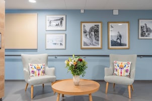A lobby with two armchairs, a round wooden table, and a vase of flowers.