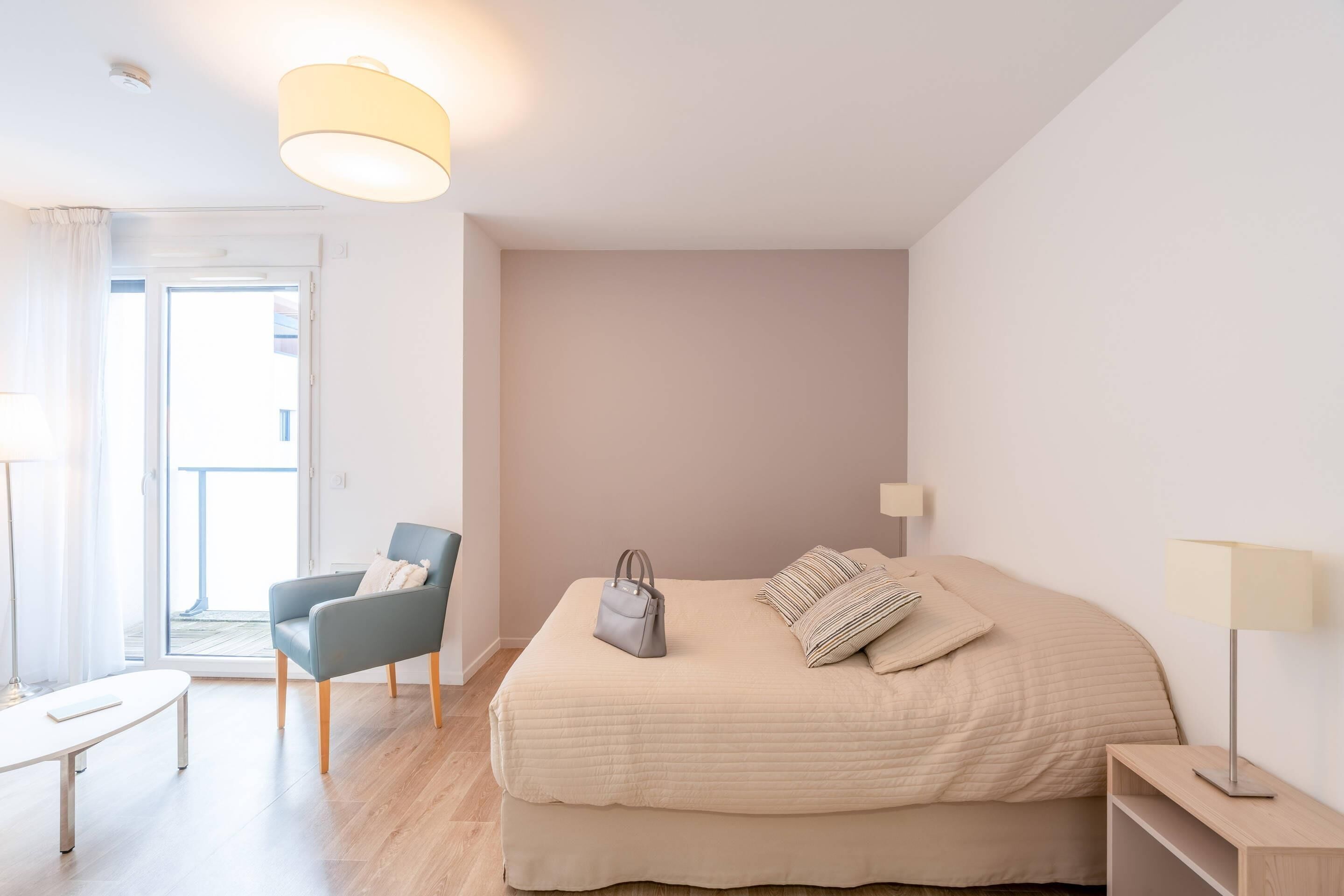 Ein Schlafzimmer mit Bett, Stuhl, Tisch und Lampe.