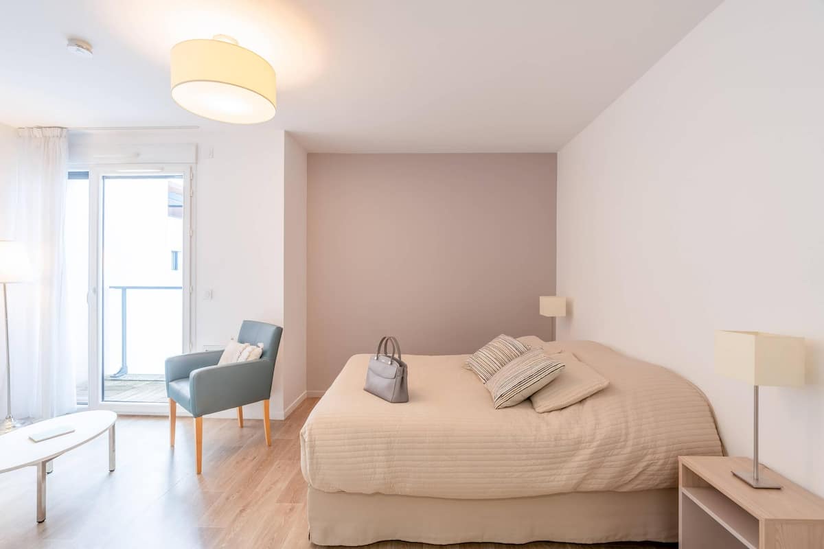 A bedroom with a bed, a chair, a table, and a lamp.