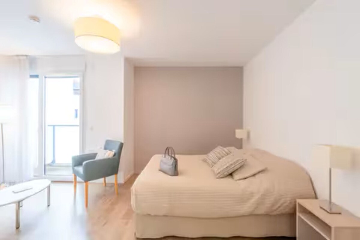 A bedroom with a bed, a chair, a table, and a lamp.