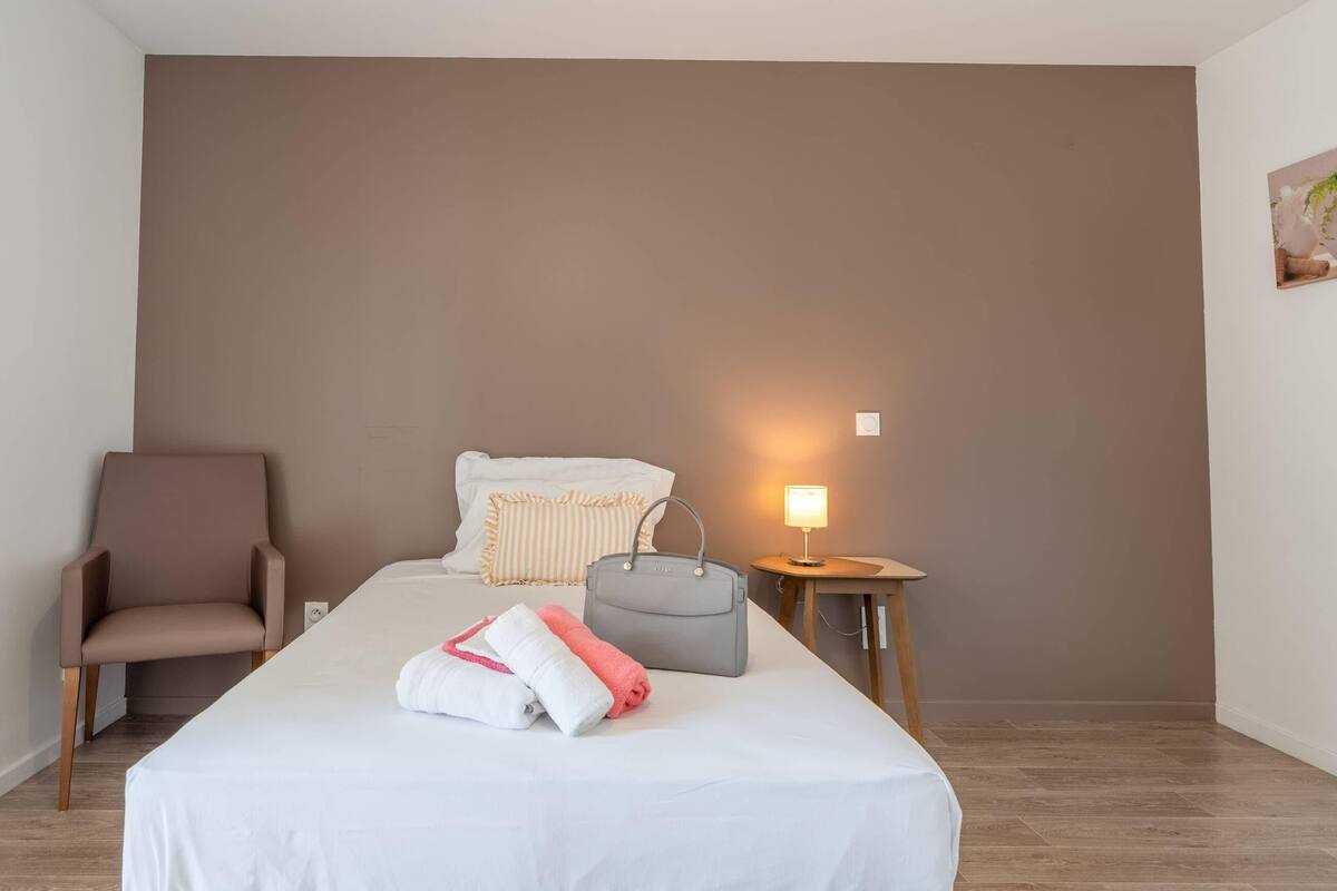 Une chambre d’hôtel avec un lit, une chaise, une table de chevet avec une lampe et une plante fixée au mur.