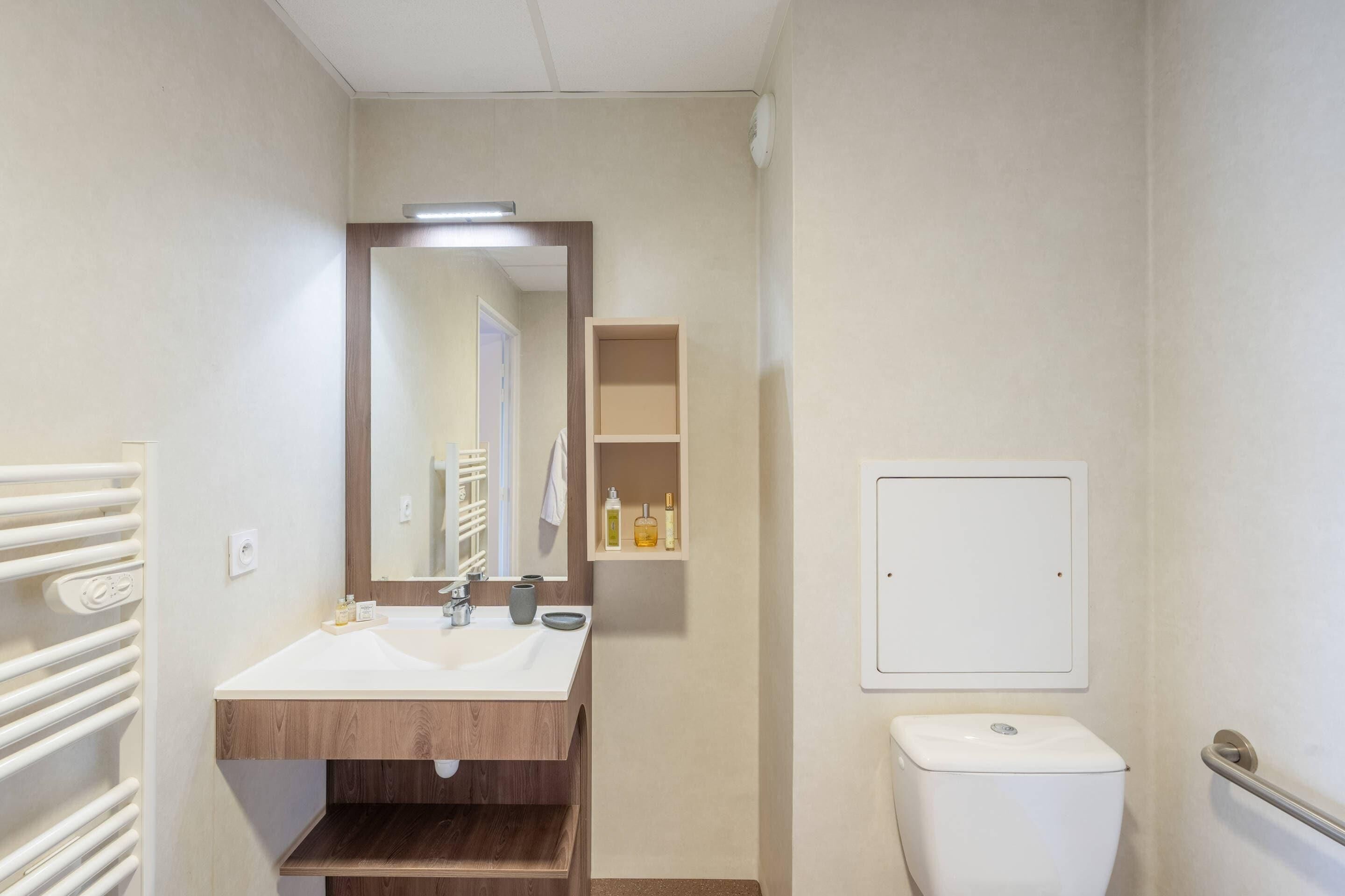 Un baño con tocador de madera, un espejo, un inodoro y un estante con artículos de aseo.