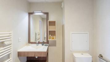Un baño con tocador de madera, un espejo, un inodoro y un estante con artículos de aseo.