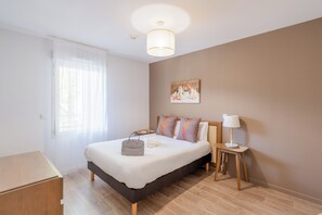 A bedroom with a bed, bedside table, lamp, and a painting on the wall. - Quality Aparthotel Lyon L'Isle-d’Abeau (L'Isle-d'Abeau)