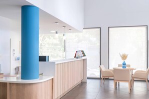 Ett modernt receptionsområde med en receptionsdisk i trä, en blå accentkolonn och en sittgrupp med två stolar och ett litet bord.