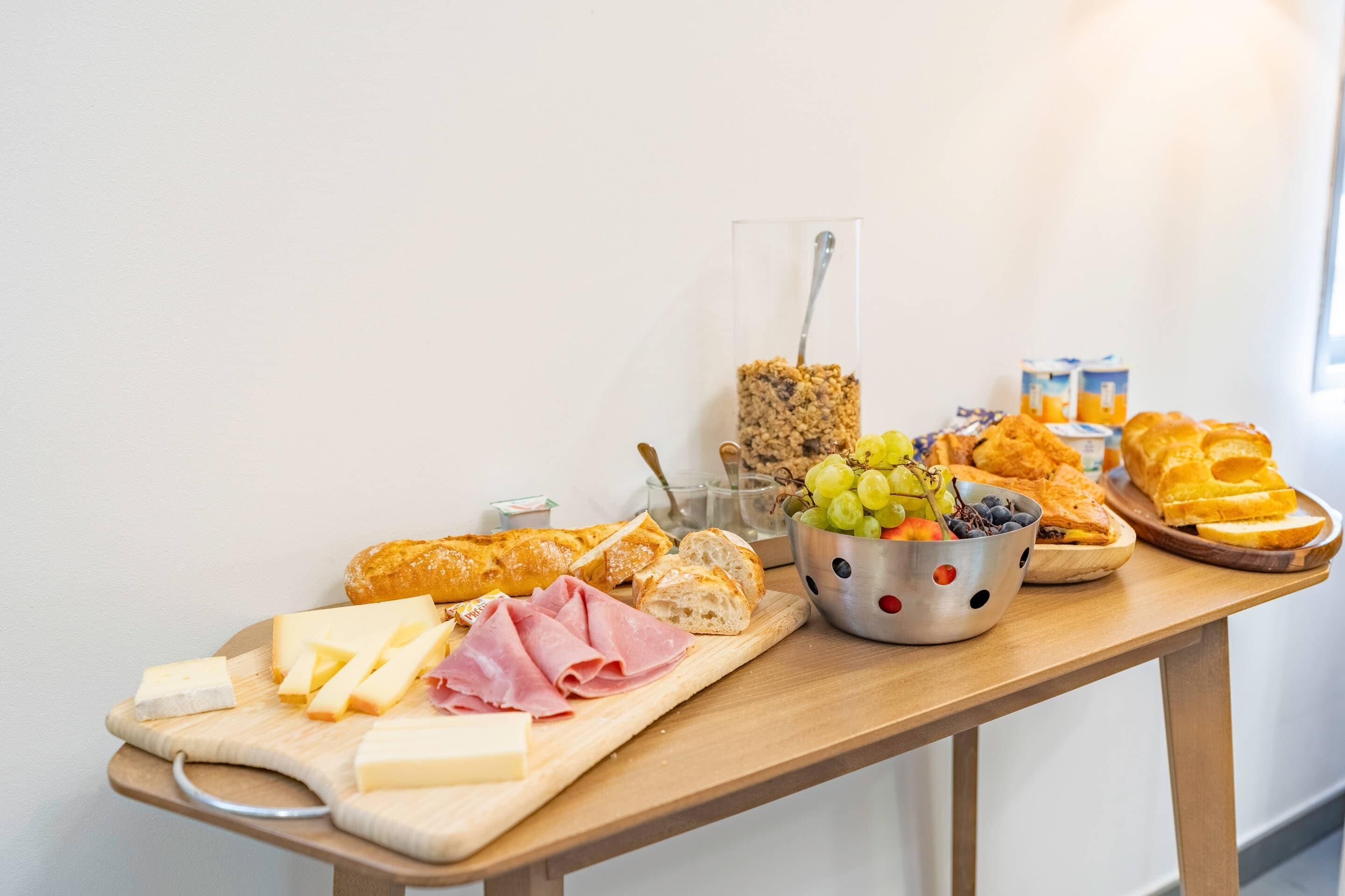A wooden table with various food items including cheese, bread, and a bowl of grapes.