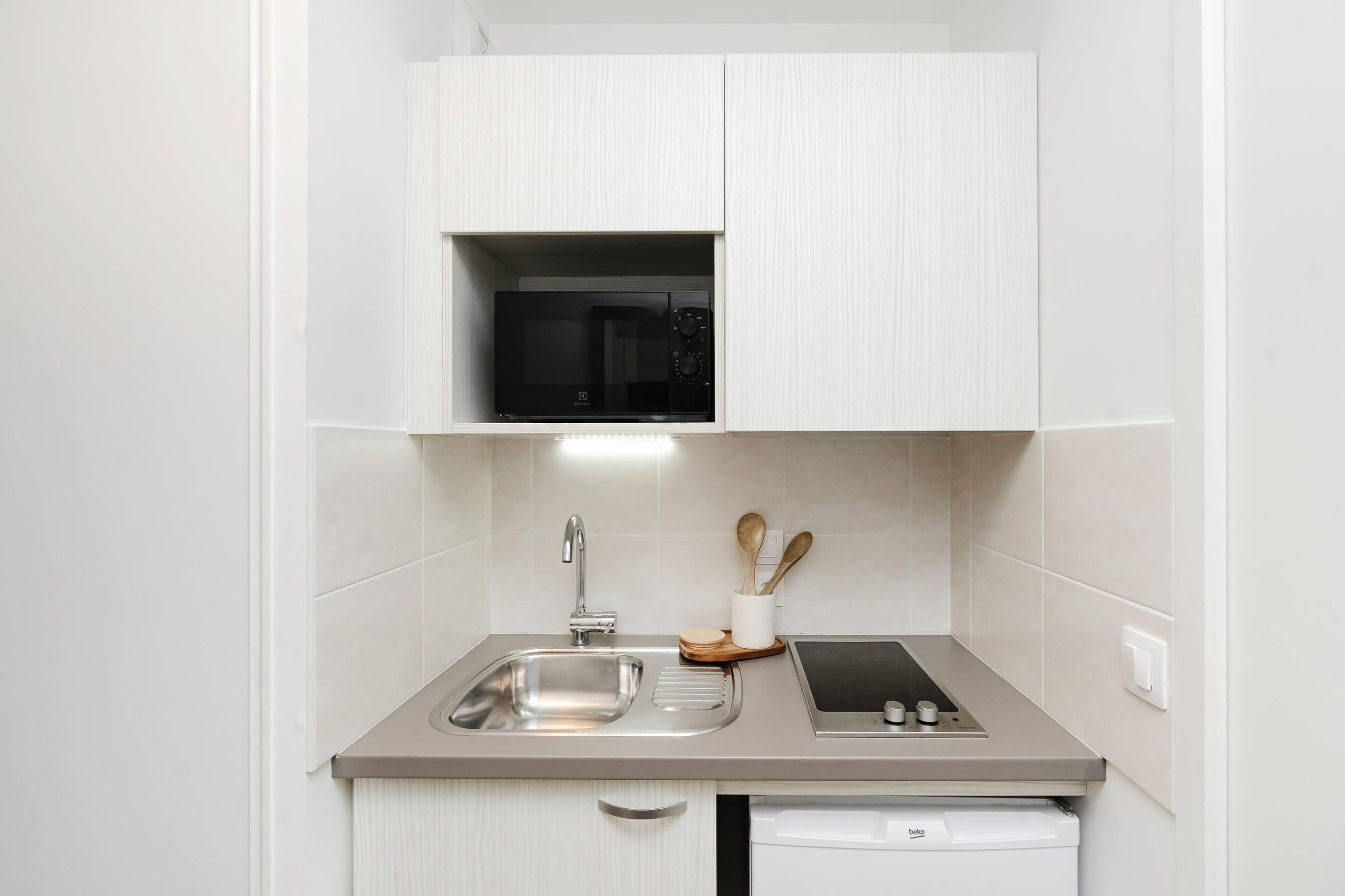 Cocina compacta con microondas integrado, pileta de acero inoxidable y una pequeña mesada con tostadora.