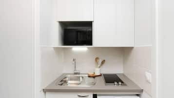 Cocina compacta con microondas integrado, pileta de acero inoxidable y una pequeña mesada con tostadora.