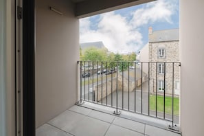 Un balcon doté d’une rambarde en métal, donnant sur un parking et des immeubles.