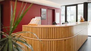 Ein Empfangstresen mit Holzoptik, eine Wand in Rot und ein gerahmtes Bild.