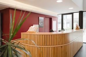 Un comptoir d’accueil avec un revêtement en bois, un mur d’accent rouge et un tableau encadré.
