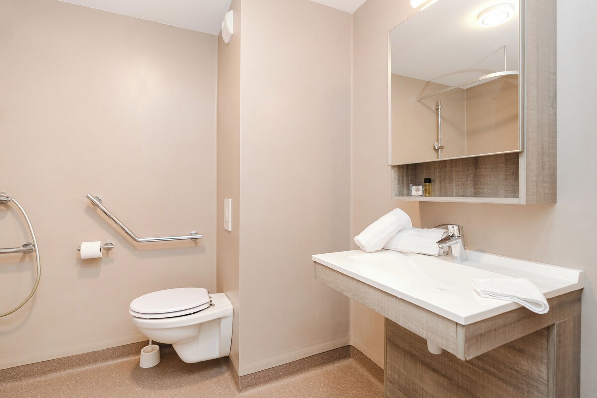 Een moderne badkamer met toilet, wastafel, spiegel en douche.