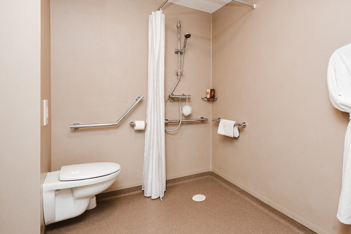 Een badkamer met toilet, een douche met gordijn, handgrepen en een handdoekhouder.