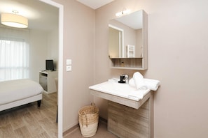 Une chambre d’hôtel moderne avec un lit, un lavabo blanc, un miroir et une armoire en bois.