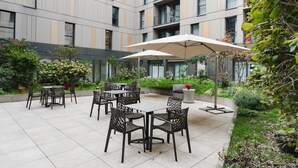 A courtyard with outdoor seating, a modern building in the background, and lush greenery. - Quality Aparthotel Saint-Malo (Saint-Malo)