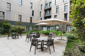 Een binnenplaats met terras, een modern gebouw op de achtergrond en weelderige begroeiing.