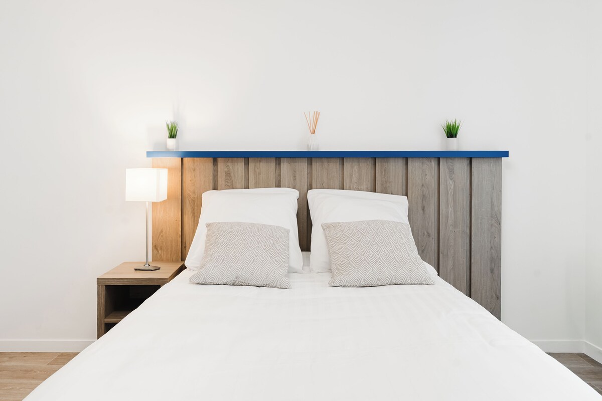 A bed with white bedding, two pillows, a nightstand with a lamp, and a wooden headboard.