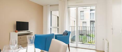 Een moderne woonkamer met een eethoek, een tv op een witte kast, en een balkon met uitzicht op de stad.