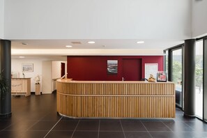 Un espace d’accueil doté d’un comptoir de réception en bois, d’un mur d’accent rouge et offrant une vue dégagée grâce à de grandes fenêtres.