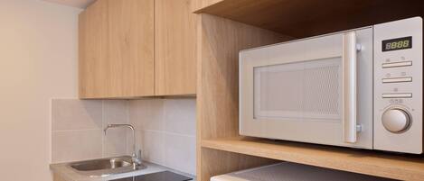 A compact kitchen with a microwave, sink, and wooden cabinets.