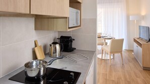 A modern kitchen with a stove, coffee maker, and utensils. There is a dining area with a table and chairs. - Quality Aparthotel Voiron (Voiron)
