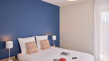 A neatly made bed with two pillows, a bedside lamp, and a book on the bed.
