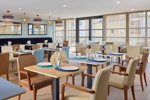 A modern dining area with multiple tables and chairs, large windows, and decorative lighting fixtures. - Quality Aparthotel Voiron (Voiron)