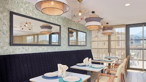 A restaurant with a dark patterned bench seating, tables with white placemats and blue centerpieces, and large mirrors on the walls. - Quality Aparthotel Voiron (Voiron)