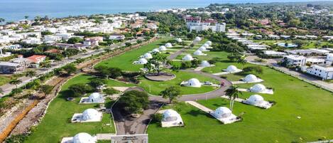 A residential area with white dome-shaped buildings, a central road, and a view of the sea.
