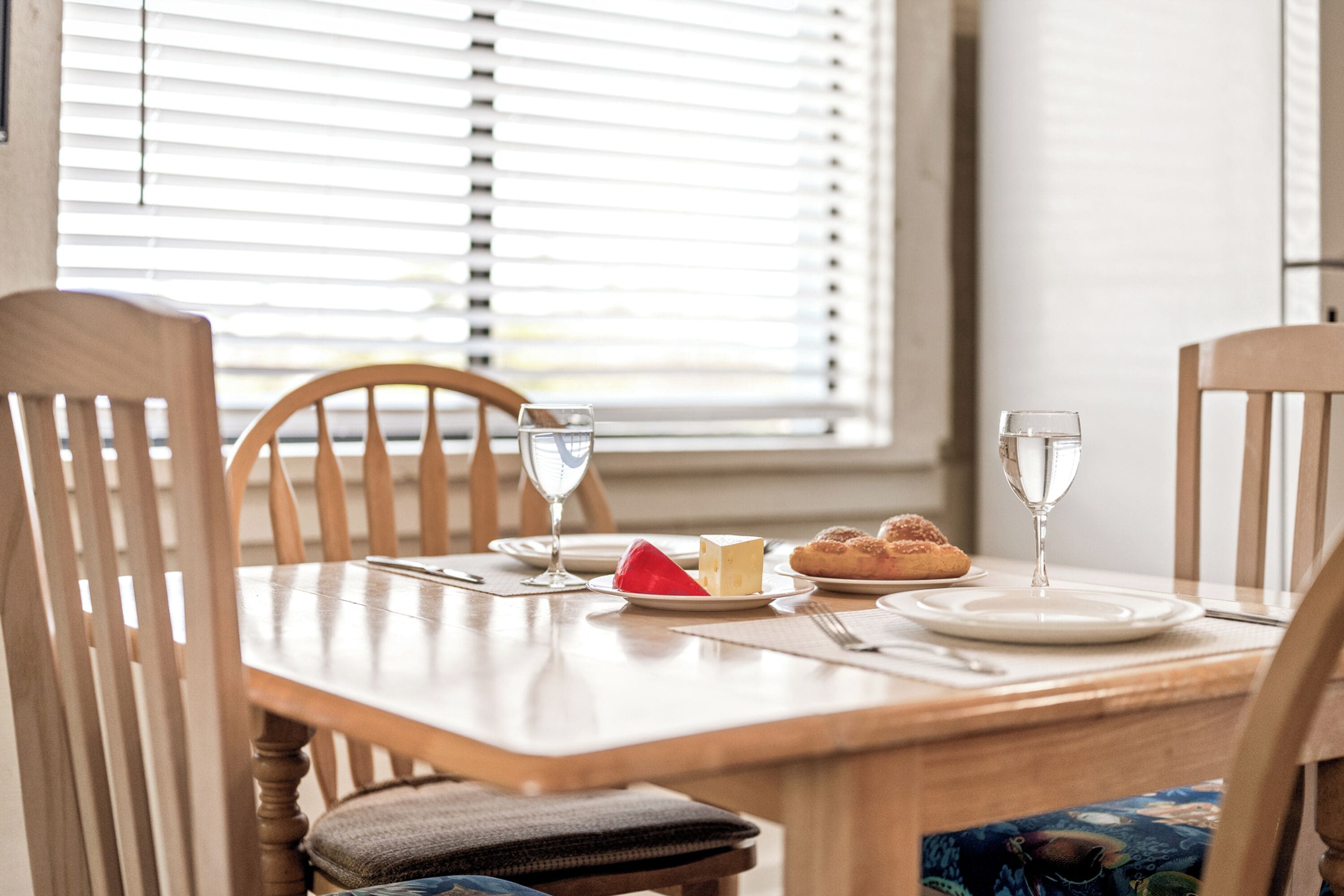 A dining table with chairs, plates, glasses, and a basket.