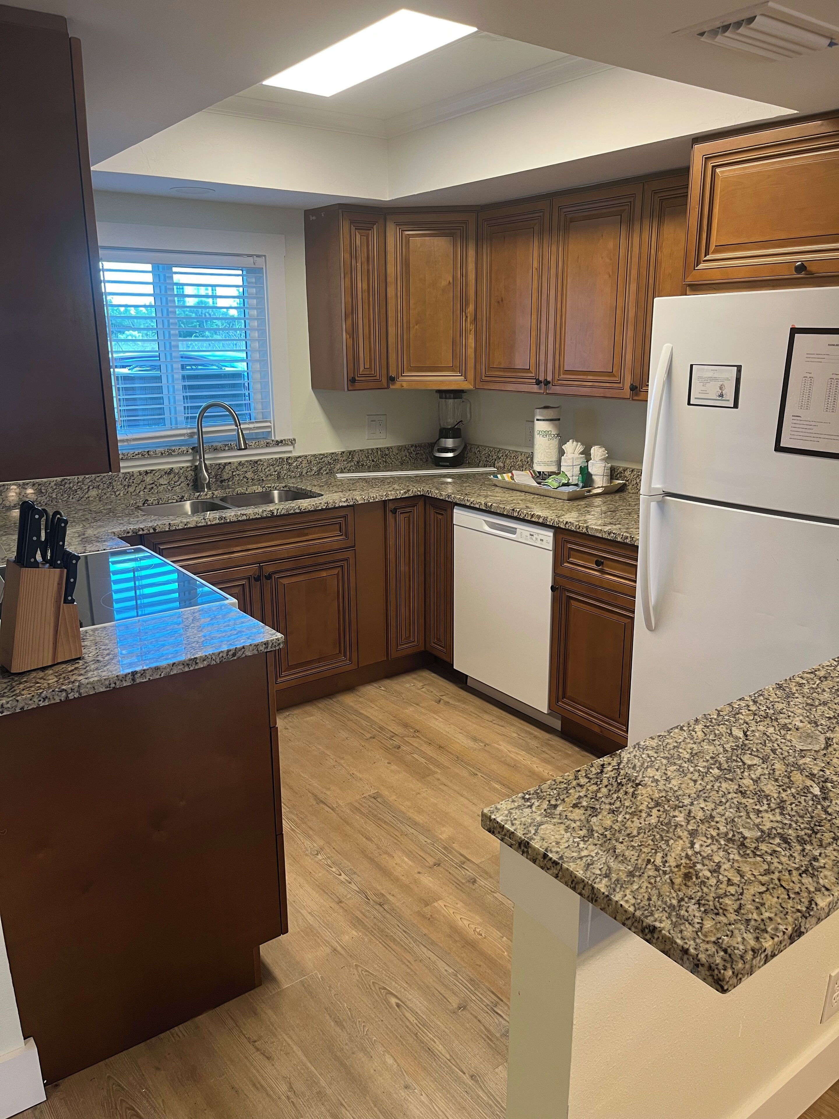 A kitchen with wooden cabinets, granite countertops, a dishwasher, and a refrigerator.