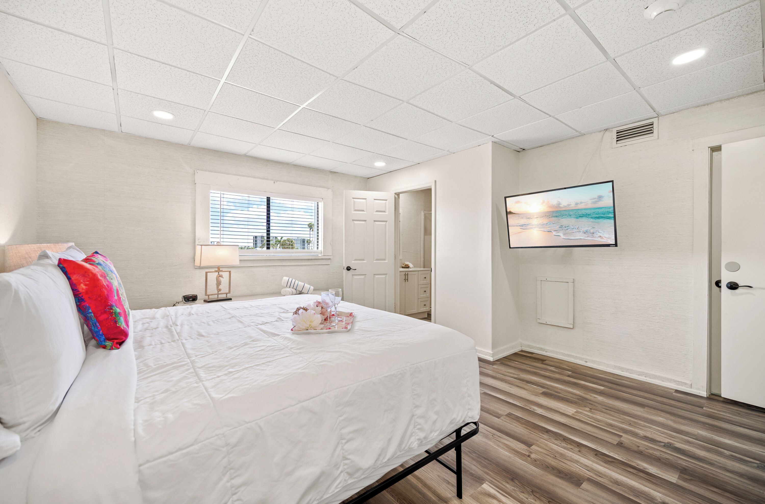 A bedroom with a bed, a window, a door, and a wall-mounted TV.
