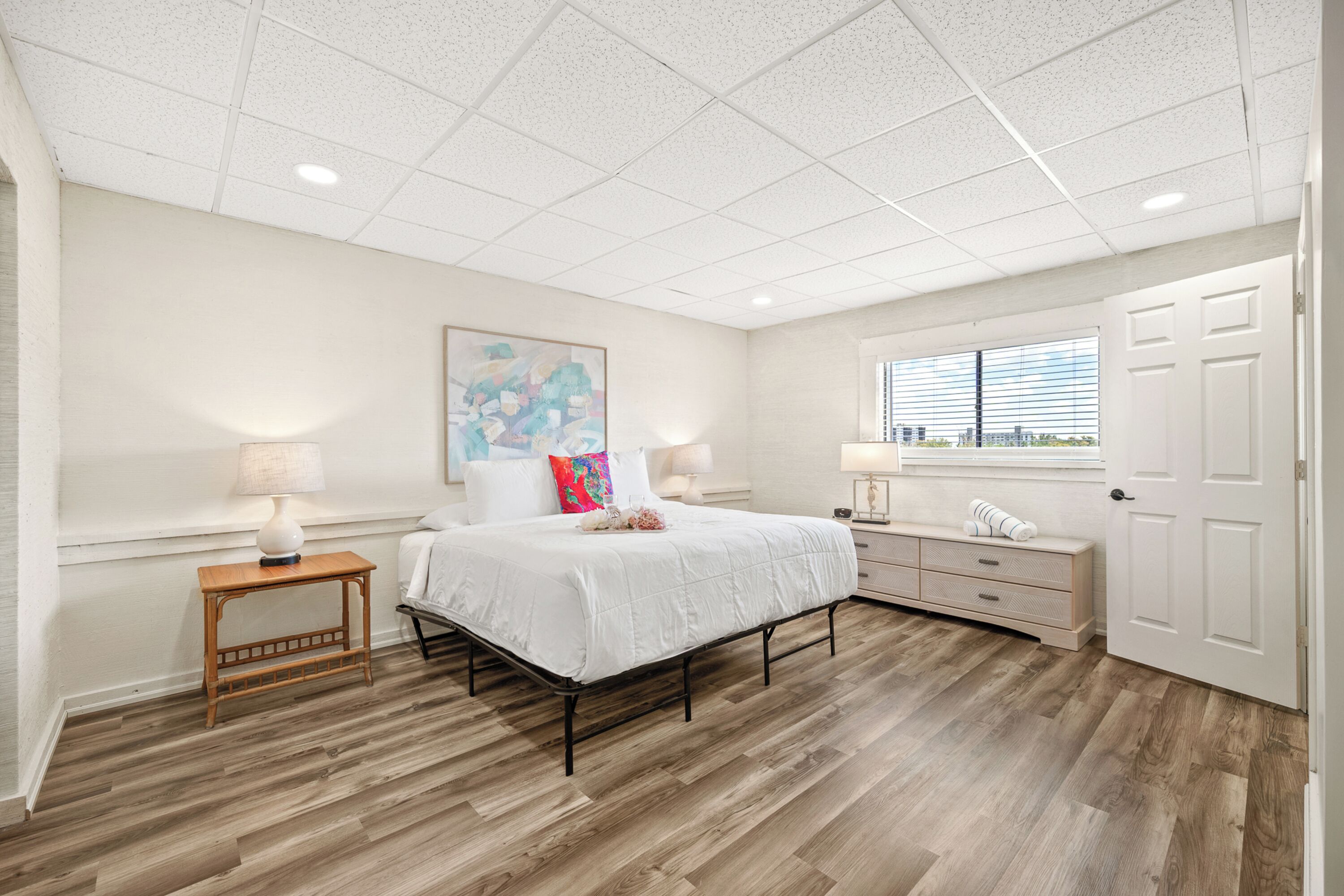 A bedroom with a bed, bedside tables, a window, and a door.