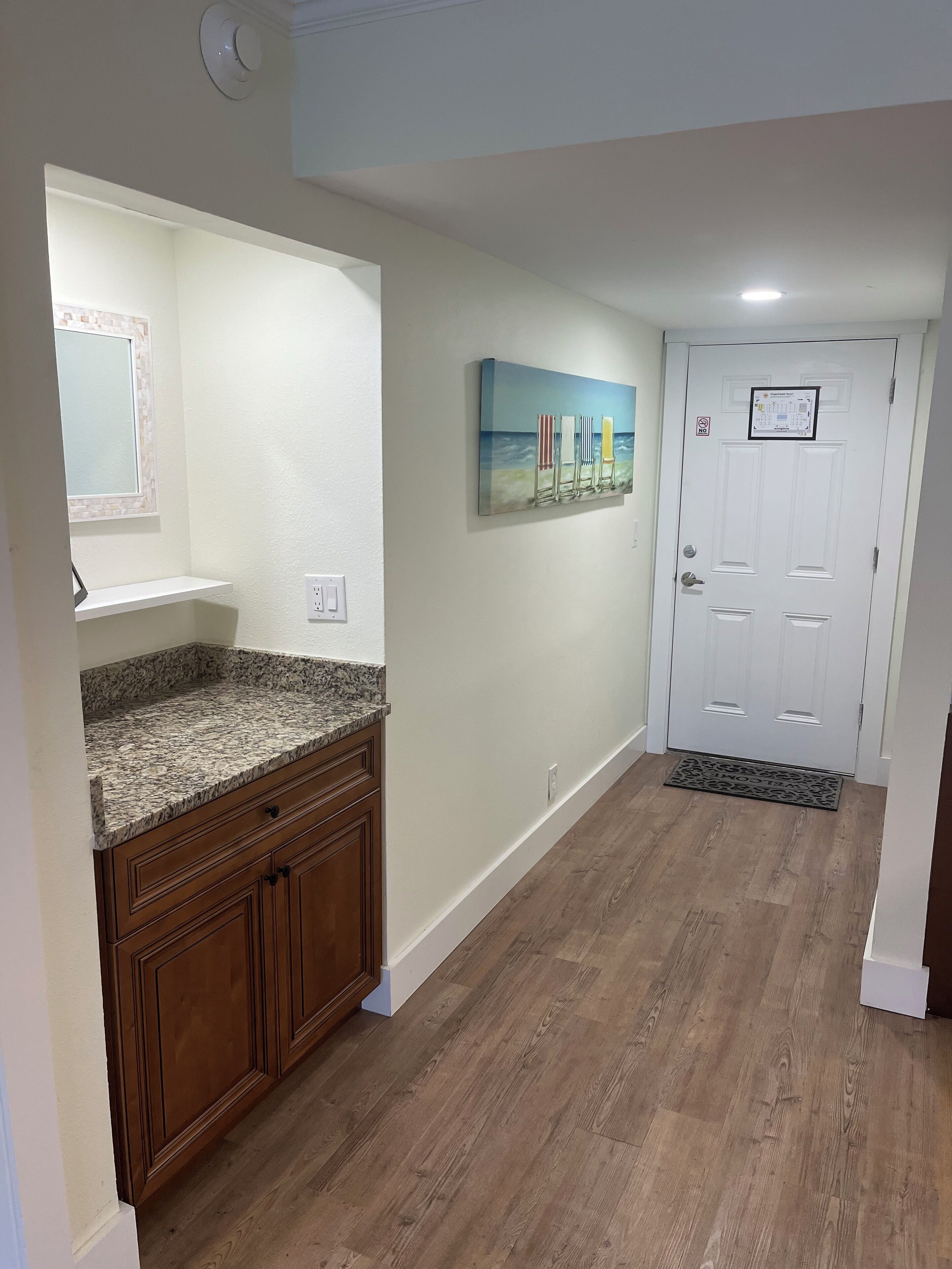 A kitchen with granite countertops, wooden cabinets, and a white door with a mat.