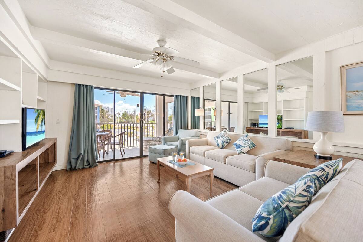 A spacious living room with a balcony, a ceiling fan, and a television.