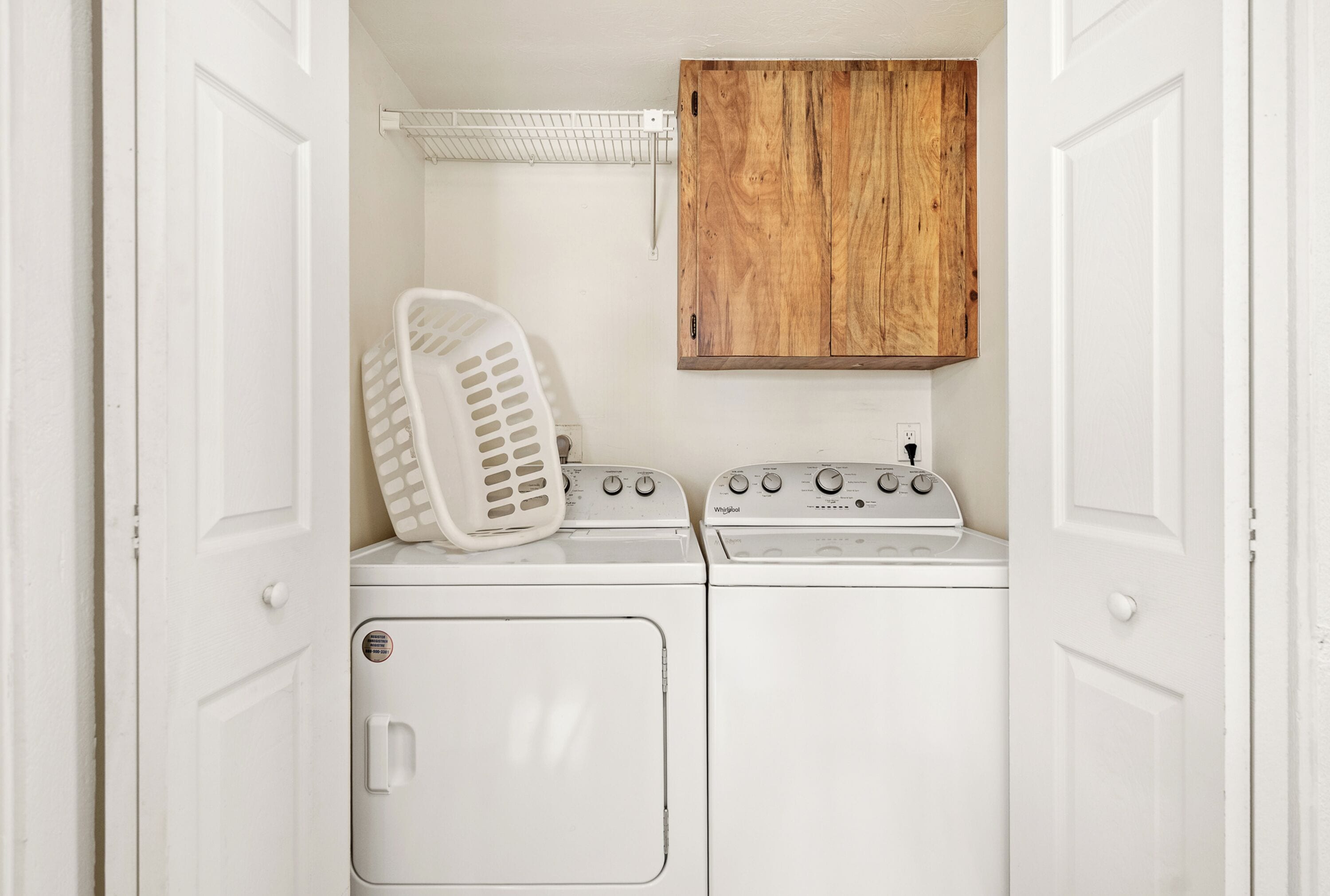 Un cuarto de lavado con lavadora y secadora, un gabinete de madera y una cesta de ropa blanca.