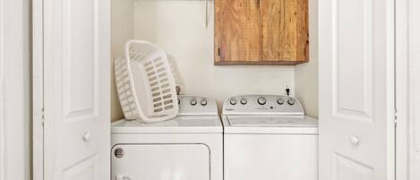 Un cuarto de lavado con lavadora y secadora, un gabinete de madera y una cesta de ropa blanca.