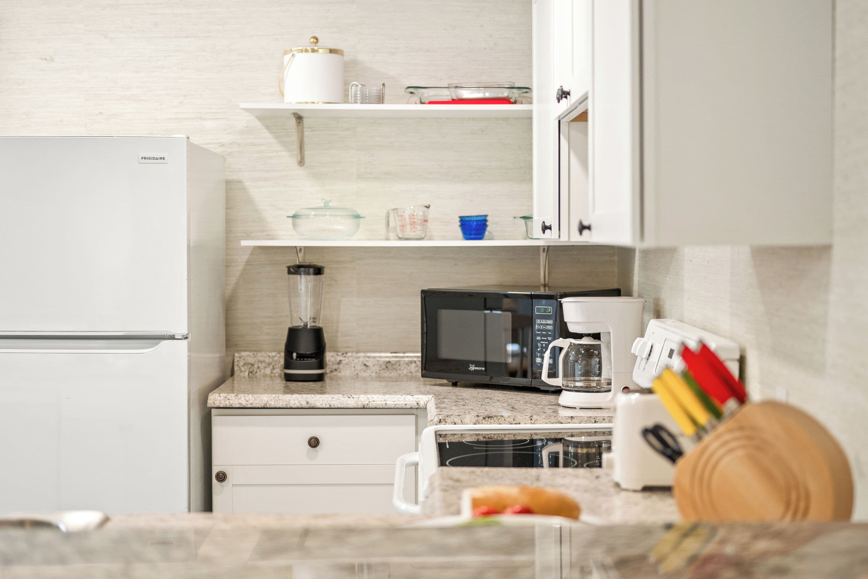 A kitchen with a refrigerator, microwave, coffee maker, and various kitchen utensils.