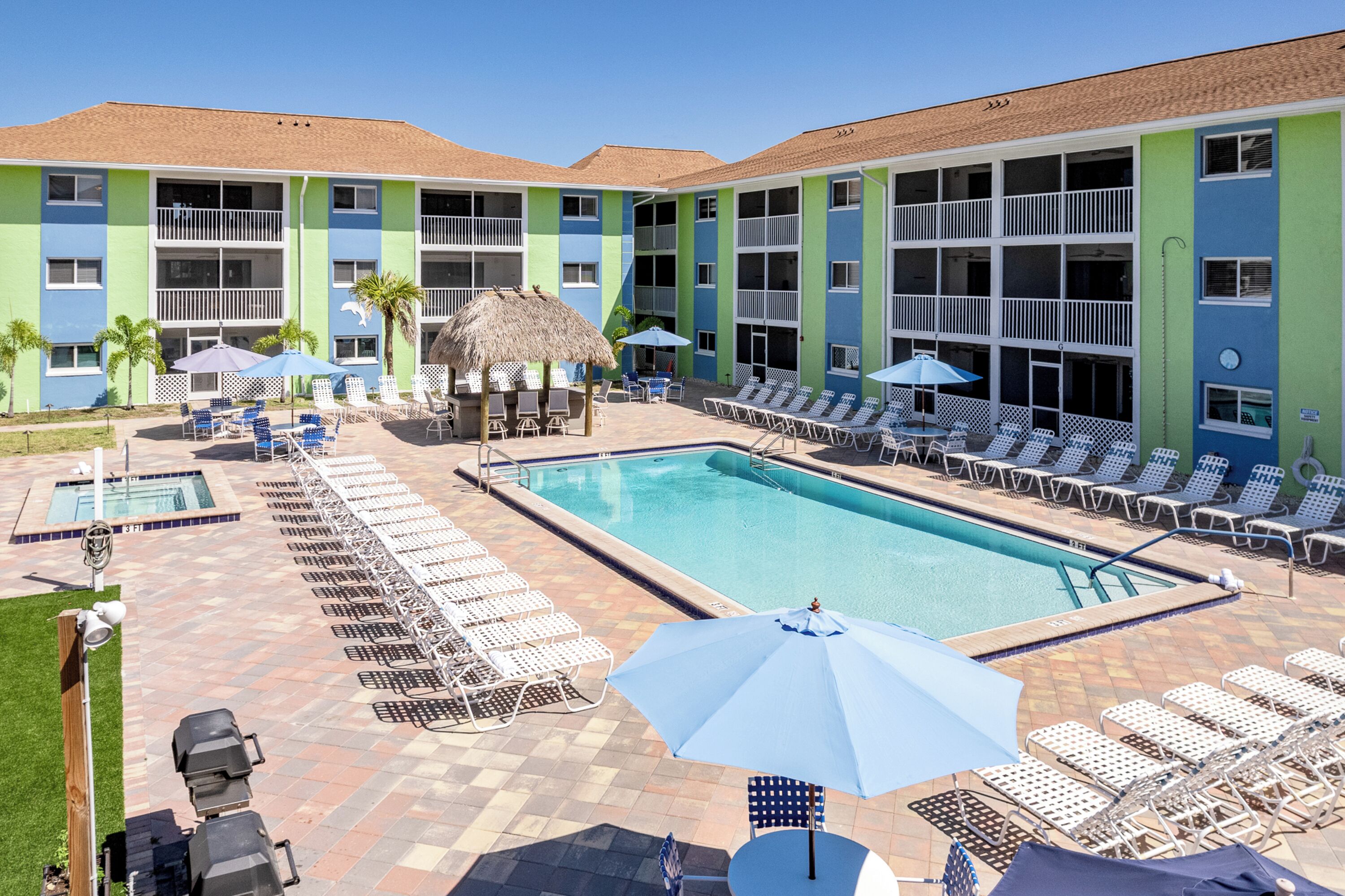 A hotel with a swimming pool, lounge chairs, and a thatched-roof structure.