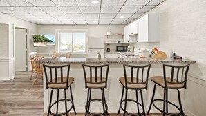 Una cocina moderna con encimera de granito, armarios blancos y tres taburetes de bar.