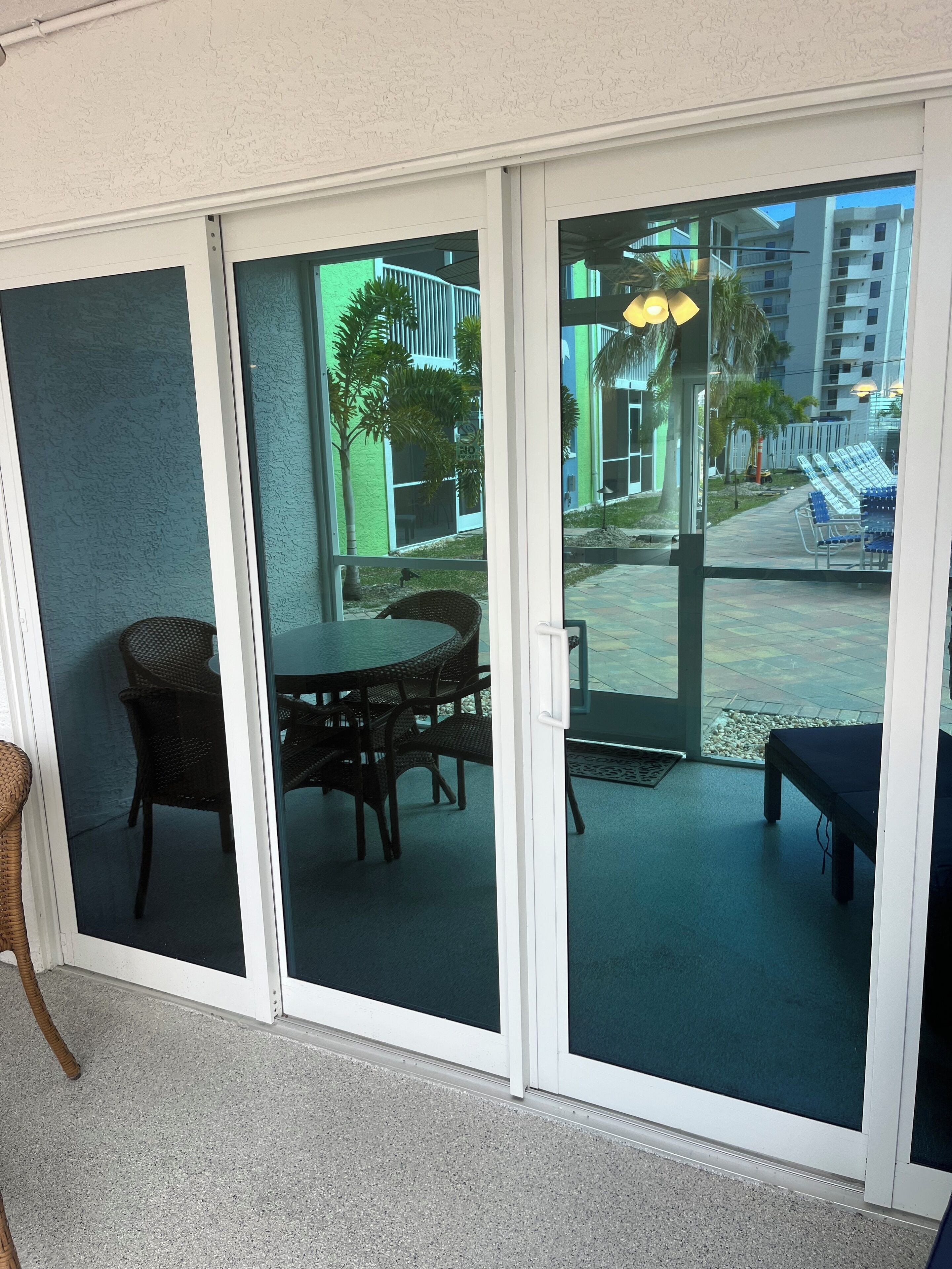 A room with a sliding glass door leading to an outdoor patio area. Inside, there is a round table with four chairs and a bench.