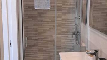 Un baño moderno con ducha de vidrio, un lavabo blanco y un espejo sobre él.