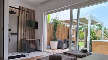 Een moderne kamer met een grote schuifdeur naar een patio. Er staat een bed met handdoeken op, een tv aan de muur en een klein tafeltje met een schaal.