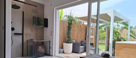 Een moderne kamer met een grote schuifdeur naar een patio. Er staat een bed met handdoeken op, een tv aan de muur en een klein tafeltje met een schaal.
