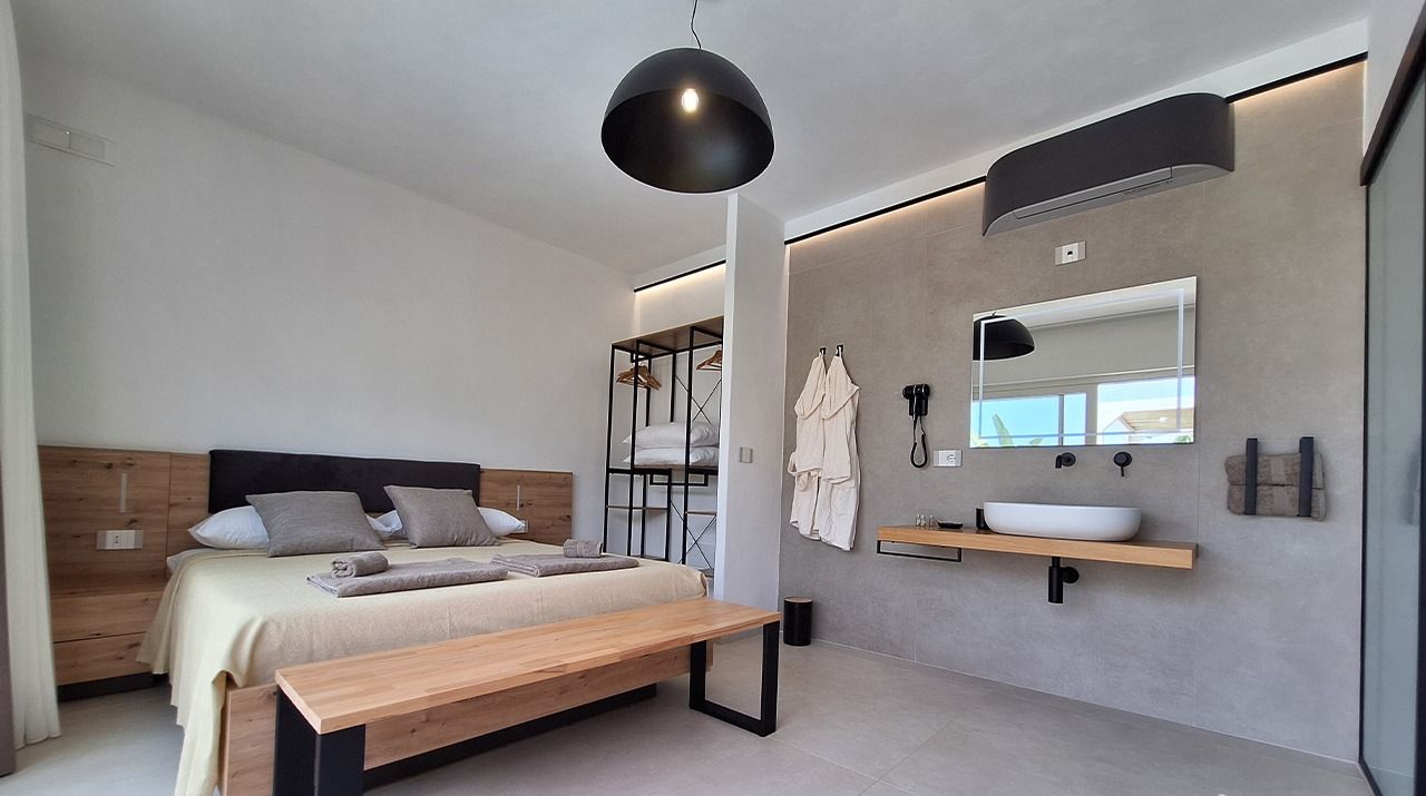 Een moderne slaapkamer met een houten bed, een bankje, een nachtkastje, een grote spiegel en een inbouwkast met een wastafel.