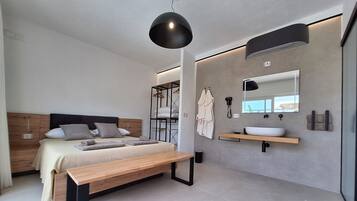 Een moderne slaapkamer met een houten bed, een bankje, een nachtkastje, een grote spiegel en een inbouwkast met een wastafel.