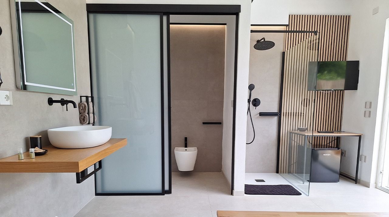 A modern bathroom with a large sink, a toilet, and a shower area. There is a wooden shelf with toiletries and a towel rack above the sink.