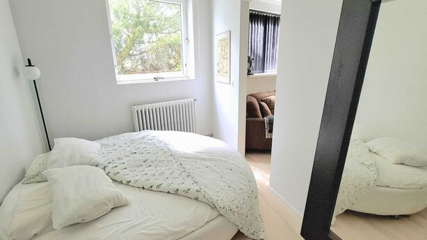 Camera da letto moderna con un letto rotondo, uno specchio grande, un termosifone e una finestra con vista sugli alberi.